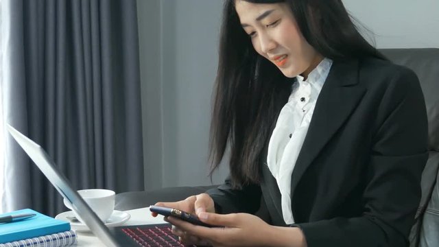 Beautiful young business woman using smartphone and smile sitting working on laptop computer in office