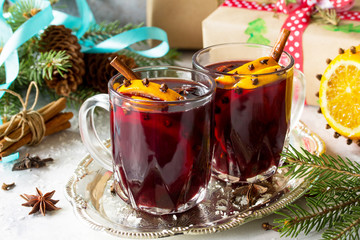 Homemade Christmas cocktail mulled wine red wine with cinnamon sticks, oranges and cloves, served in two cups on a gray stone or slate.