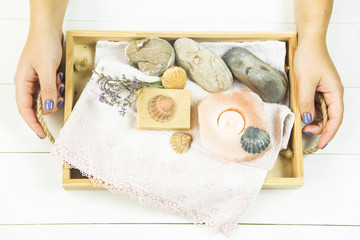 the girl is holding a wooden tray with accessories for spa procedures with a floppy, candles and soap. Flat lay. Top view