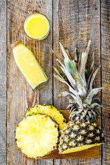 Freshly squeezed pineapple juice near fruit slices on wooden background top view