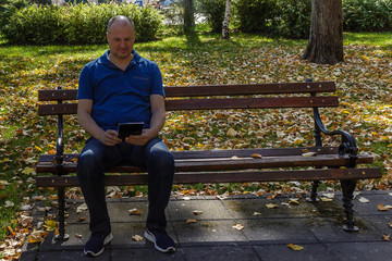 Man in blue shirt reading with digital tablet on a park bench