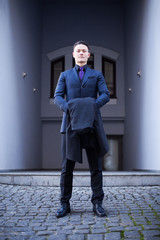 A wealthy, confident and successful businessman in a business suit stands at the entrance of his own house. Vertical portrait.