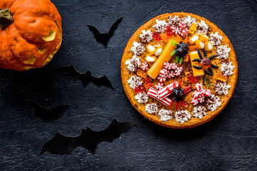 Halloween tradition. Pumpkin pie, pumpkin with carved face and bats on black background top view