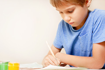 Boy painting with paintbrush and colorful gouache and watercolor paints.