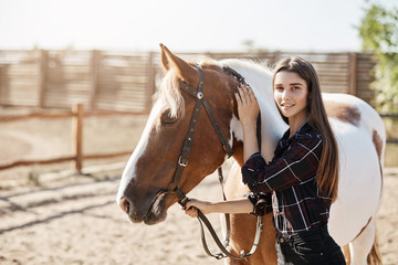 Obraz premium Young female veterinarian calming down an ill horse looking at camera smiling.