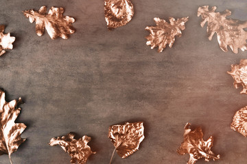 Frame made of fall rose gold colored leaves on dark table from above. Creative concept. Copy space for text