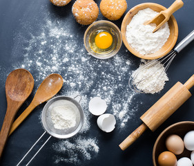 Baking ingredients. Bowl, eggs, flour, eggbeater, rolling pin and eggshells on black chalkboard from above.