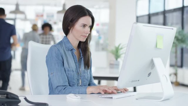  Portrait smiling young woman working on computer in creative office with colleagues talking in background. Shot on RED Epic.