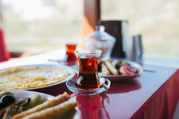 A cup of hot fragrant black tea. Two plates with vegetarian food - fresh vegetables and cheese, cake and drink in glass on red table