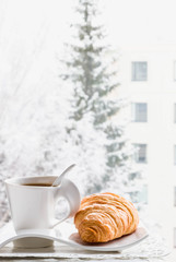 Hot Coffee cup with croissant on a frosty winter day window background