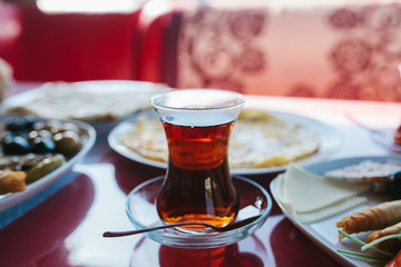 A cup of hot fragrant black tea. Two plates with vegetarian food - fresh vegetables and cheese, cake and drink in glass on red table