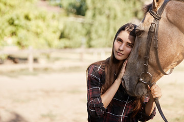 Portrait of young woman and a horse. Longhaired beautiful girl holding and calming down a stallion.