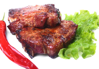 Steak of grilled meat and chili pepper with tomato, lettuce leaves on white plate.