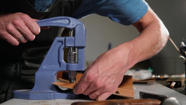 Craftsman using riveting machine to fix the snaps on the handmade leather cover for notebook