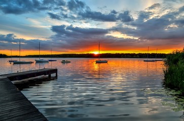 Naklejka na ściany i meble Beautiful summer evening landscape. Wooden pier and boat on the lake at sunset.
