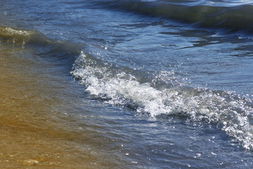 Soft waves on a sandy seashore. Sea beach on a sunny day, blue ocean water. Selective focus