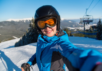 Close-up portrait of happy woman skier smiling, taking a selfie while resting on the slope after skiing in the Carpathians mountains at ski resort on a beautiful sunny winter day Bukovel, Ukraine