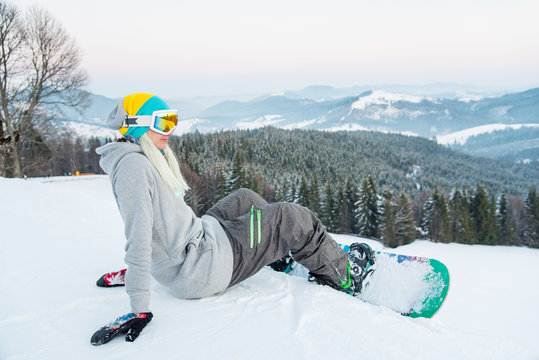 Shot of a cheerful young female snowboarder sitting on the snow, having fun outdoors, resting in the mountains after riding happiness recreation winter sports concept