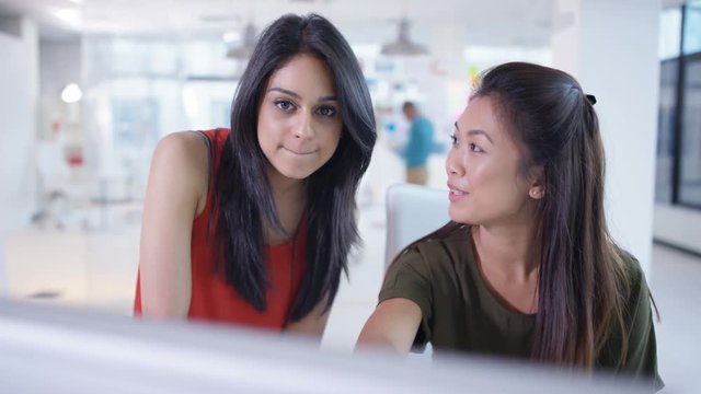  Young businesswomen looking at computer & collaborating in creative office