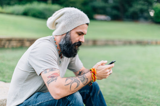 Tattooed man in a hat using a smartphone
