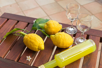 Lemonade or limoncello in a glass bottle, glasses, lemons with leaves on a wooden table. Close-up.