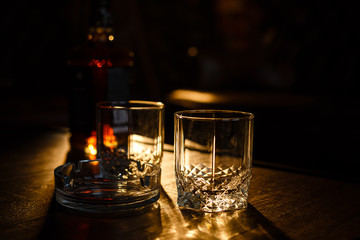 Glasses of whiskey with smoking cigar and ice cubes on wooden table