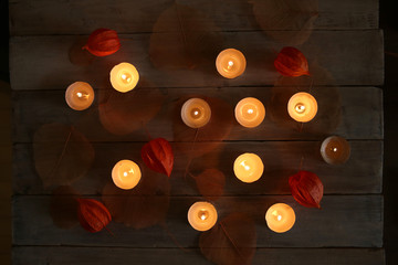 Burning candles with plant decorations  in the darkness. Small round tea light candles with chinese lanterns and leaves on wooden table top view.