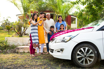 Indian family buying new car - Car buying or automobile boom concept in india, image representing asian family performing Pooja of newly purchased car or four wheeler at home wearing ethnic cloths

