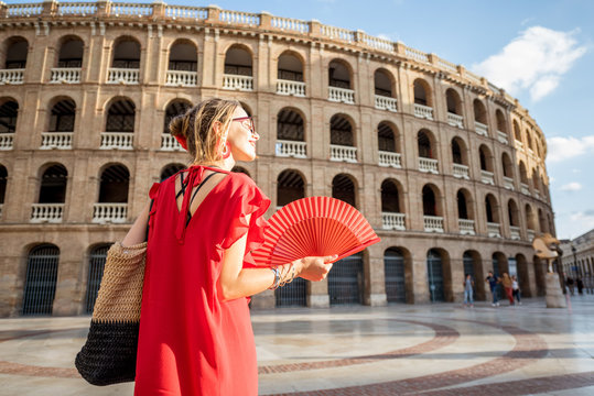 Woman in red dress with spanish hand fan stnading back in front of the bullring amphitheatre in Valencia city, Spain
