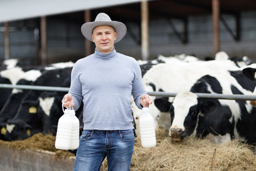 positive farmer with milk containers on background of cow farm