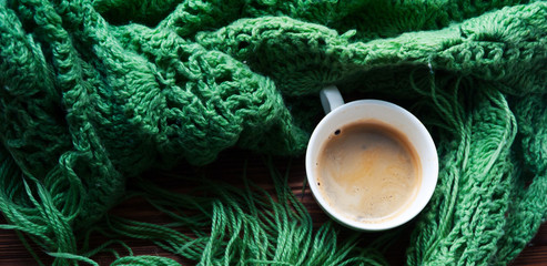 the panorama of top view of cup of hot coffee and warm green scarf. Concept of coziness and warmth