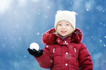 Adorable little girl having fun in beautiful winter park. Cute child playing in a snow.