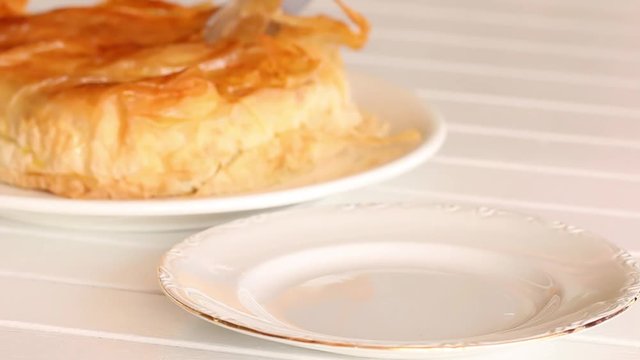 A knife cut a slice of filo pastry timbal and put it in a plate.