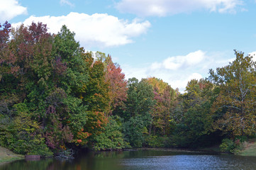 Landscape photo of a small lake in the country lined with trees showing their Autumn colors