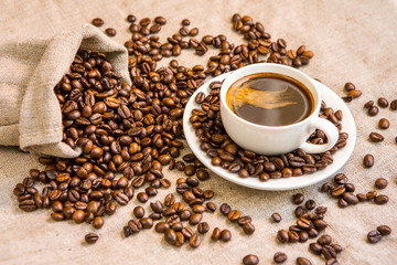 Bag of coffee beans and a cup of coffee on the table. Sackcloth.