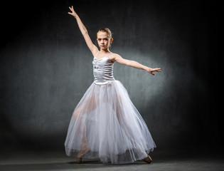 Fototapeta na wymiar Beautiful young ballerina is dancing in the studio on a dark background. A little dancer. Ballet dancer.