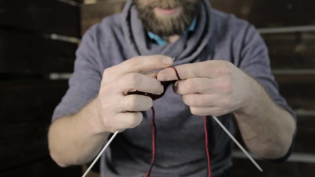 close-up hands with knitting needles, bearded man trying to knit