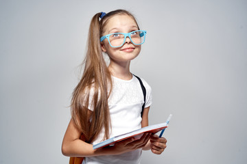 little schoolgirl with glasses in hand notebook on gray background, study, school