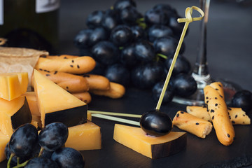 Cheese plate served with crackers, grapes and glass of white wine on dark background.