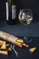 Cheese plate served with crackers and glass of white wine on dark background.