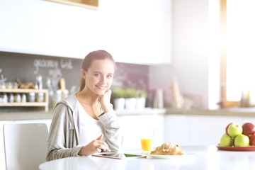 Young woman with orange juice and tablet in kitchen.