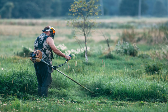 Farmer cutting grass with string trimmer in a meadow
