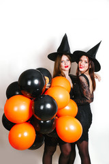 Two happy sexy women in black witch halloween costumes with orange and black balloon on party over white background