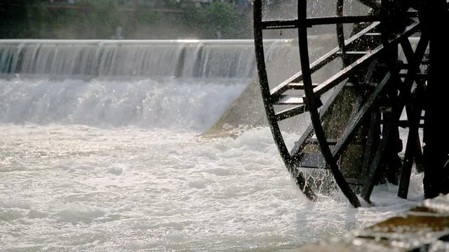 Handheld shot of water mill wheel on river on sunny day in Fenghuang Ancient Town, Guanxi County, China. Sustainable energy and water power traditional machinery, eco-friendly technology concept.