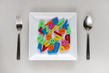 Alphabets in a white plate with a spoon and a fork.