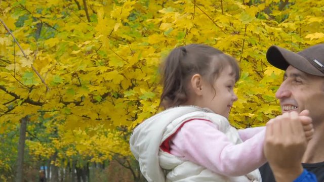 A father with a little daughter is dancing in an autumn park.