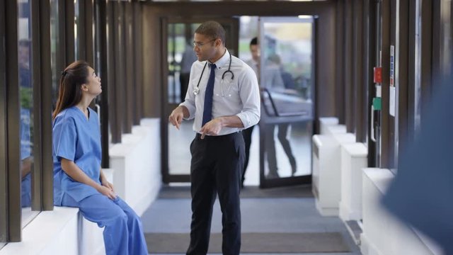  Doctor & nurse having a discussion in busy hospital corridor.