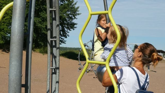 Mother walking with kids and playing on sandy playground