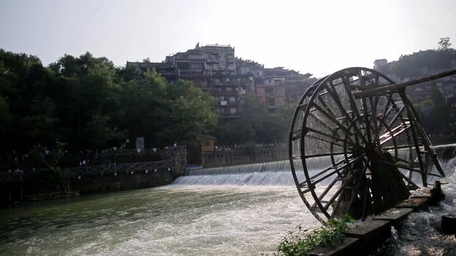 Handheld shot of water mill wheel on river on sunny day in Fenghuang Ancient Town, Guanxi County, China. Sustainable energy and water power traditional machinery, eco-friendly technology concept.