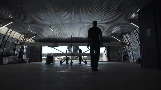 Person walking towards plane standing in hangar, view from behind.